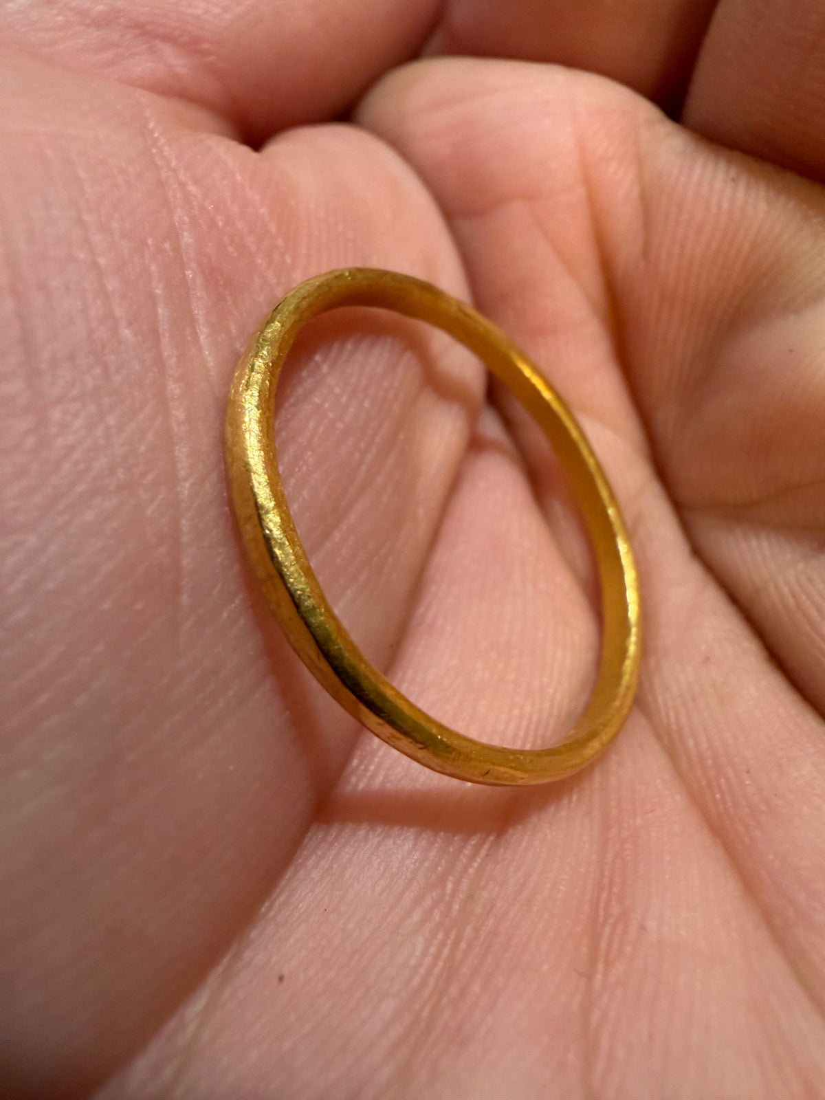 Thin solid 24k gold band held up between fingers